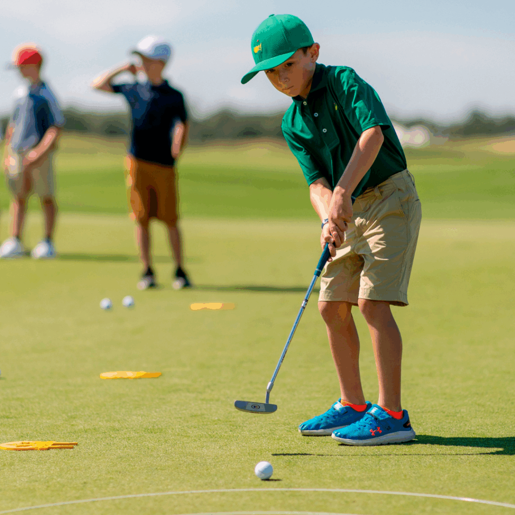 Niño practicando putt en clase de golf infantil en el green acompañado de compañeros